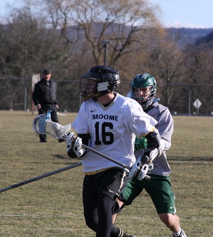 Broome lacrosse player with ball, chased by opponent